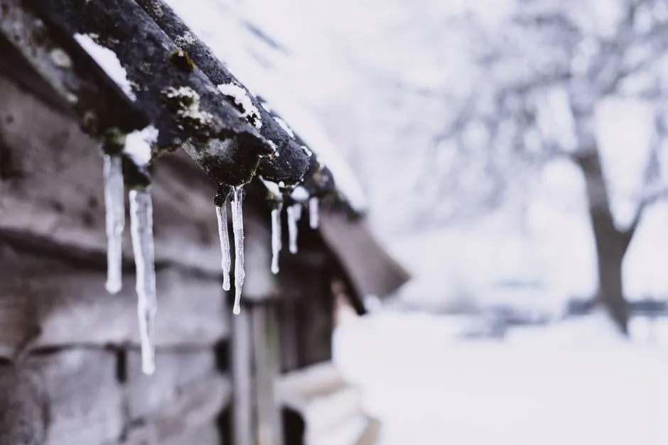 Close-up of icicles on a wooden roof in a snowy winter setting, outdoors.